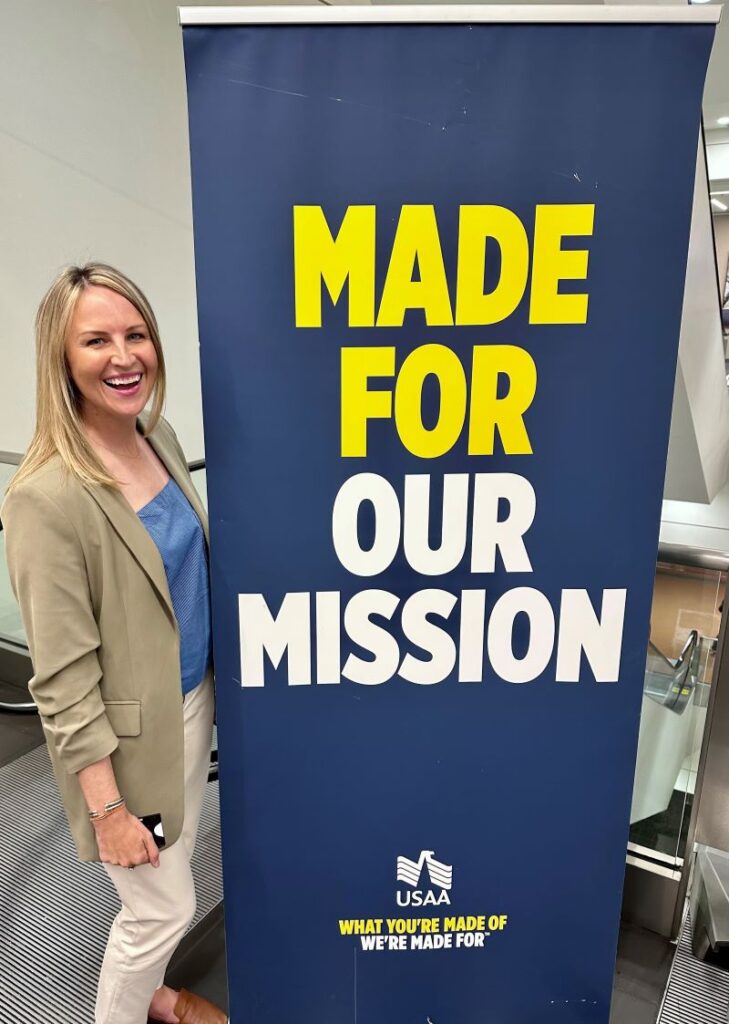 USAA employee stands by sign USAA hosts military spouses to be fellows through Hiring Our Heroes.